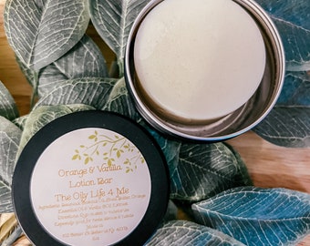 May include: A black and white label on a round container reads "Orange & Vanilla Lotion Bar The Oily Life 4 Me" with ingredients and directions listed below. The container is open and a white lotion bar is visible inside.