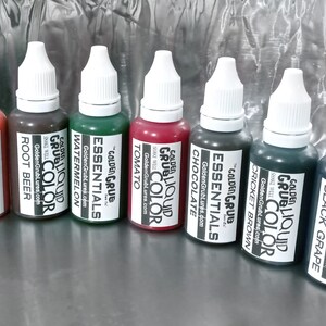 May include: Eight small bottles of liquid colour for use in crafting and art projects. The bottles are labelled with the colour names: Orange Craw, Root Beer, Watermelon, Tomato, Chocolate, Cricket Brown, Black Grape. Each bottle has a white cap and a label with the Golden Grub logo.