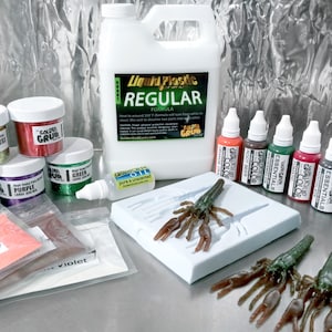 May include: A set of craft supplies for making fishing lures, including liquid plastic, glitter, colorants, and a mold for a crawfish lure. The set also includes a bottle of pure and unscented oil. The text on the bottle of liquid plastic reads "Liquid Plastic Regular Formula".