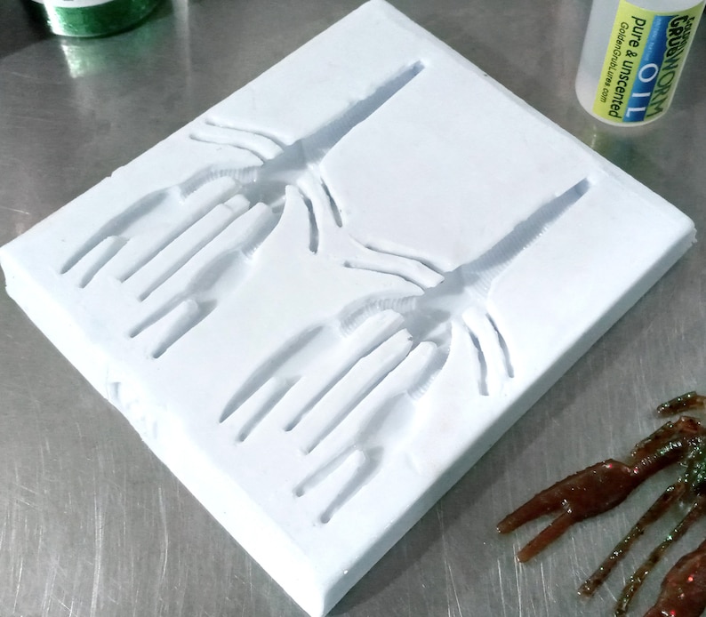 May include: A white silicone mould with two impressions of a crawfish or crayfish. The mould is on a silver surface.