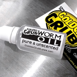 May include: A clear plastic bottle with a white dropper top. The bottle is labelled "Golden Grub Worm Oil, pure & unscented, GoldenGrubLures.com".
