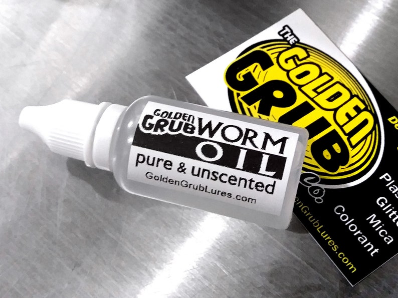 May include: A clear plastic bottle with a white dropper top. The bottle is labelled "Golden Grub Worm Oil, pure & unscented, GoldenGrubLures.com".