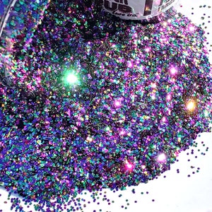 May include: A close-up of iridescent glitter in a variety of colors, including purple, green, gold, and blue. The glitter is scattered on a white surface.