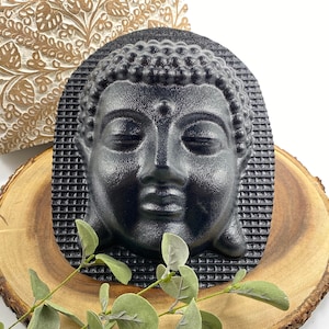 May include: Black Buddha head mold made of silicone. The mold is textured and has a detailed design.