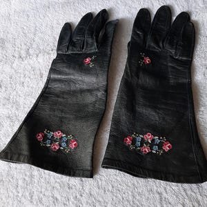 May include: A pair of black leather gloves with embroidered floral details in pink, blue, and green.