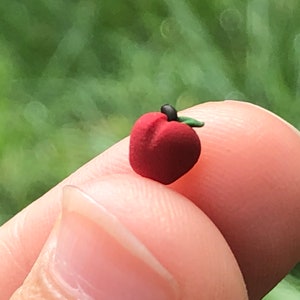 May include: A small, red, clay apple with a green leaf and a black stem.