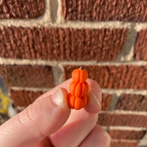 Op de afbeelding: Een stapel van drie kleine oranje pompoenen, elk met een iets andere vorm en grootte.