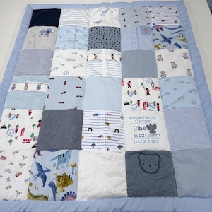 May include: A patchwork baby quilt with a pale blue border. The quilt is made from squares of fabric in blue, white, and grey, with patterns such as stripes, spots, and animal motifs. One square displays the baby's name, weight, and date of birth.