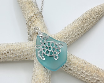 May include: A silver turtle pendant necklace with a light blue sea glass charm. The necklace is displayed on a white starfish.