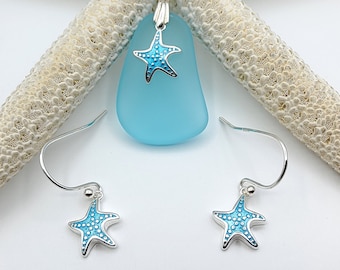 May include: A silver necklace and earrings set featuring a starfish design with blue accents. The necklace pendant is a light blue sea glass shape. The jewelry is displayed on a white starfish against a white background.