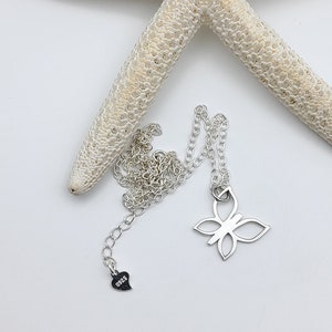 May include: A silver butterfly necklace with a heart charm that says "925". The necklace is on a white background with a starfish.