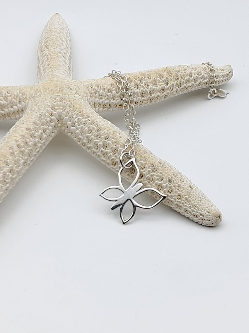 May include: A silver butterfly charm necklace with a delicate chain. The necklace is displayed on a white starfish.