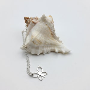 May include: A silver butterfly pendant necklace with a delicate chain. The necklace is displayed on a white seashell.