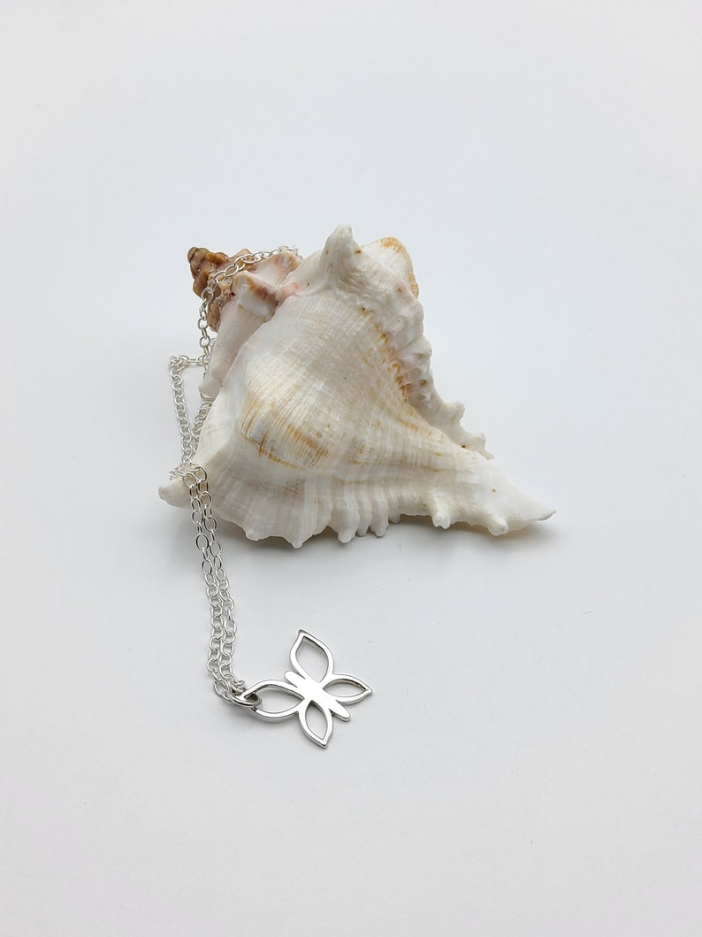 May include: A silver butterfly pendant necklace with a delicate chain. The necklace is displayed on a white seashell.