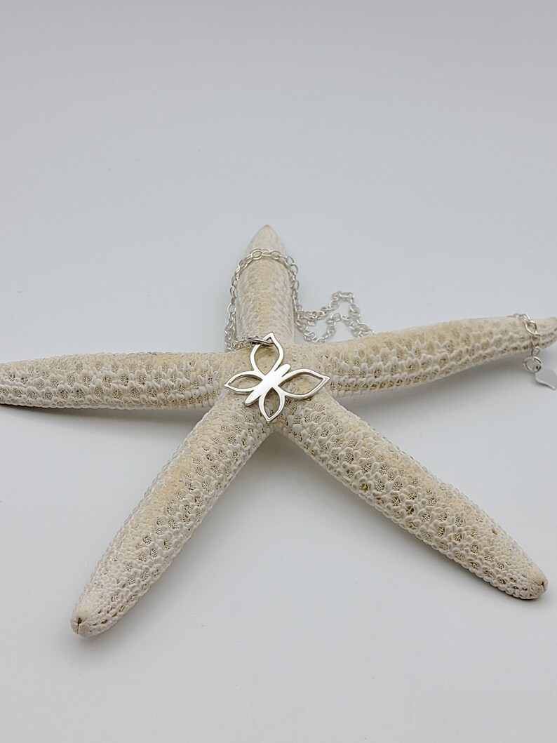 May include: A silver butterfly pendant necklace on a white starfish. The pendant is a delicate, openwork design.