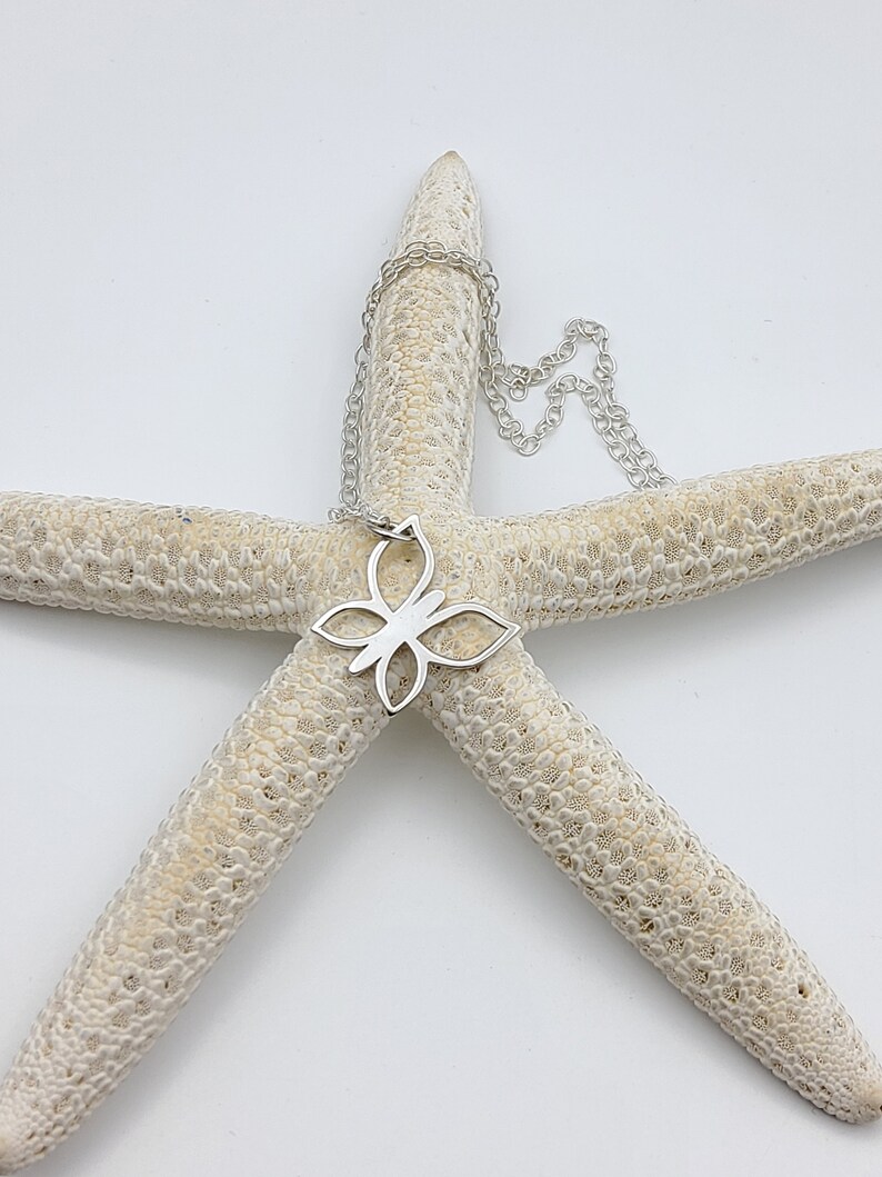 May include: A silver butterfly pendant necklace on a white starfish background.