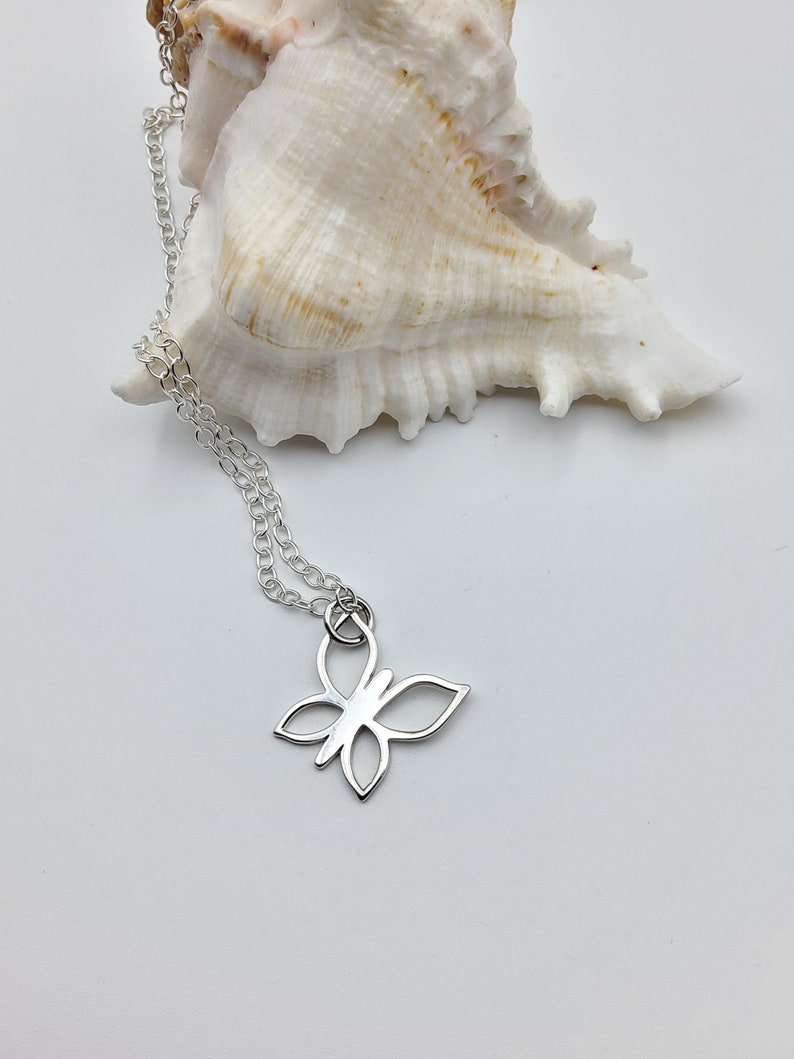 May include: A silver chain necklace with a delicate butterfly pendant. The pendant is a simple outline of a butterfly with open wings.