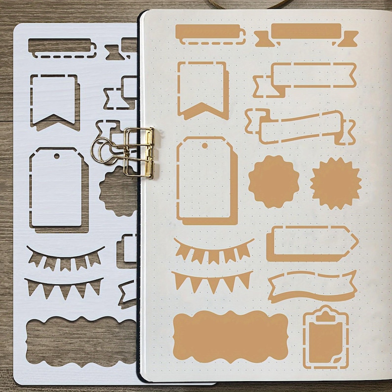 Puede incluir: Una plantilla blanca con varias formas para hacer un diario, incluyendo etiquetas, pancartas y bordes decorativos. Un clip dorado sujeta la plantilla y una p&aacute;gina de diario con formas a juego en color beige. La p&aacute;gina del diario tiene una cuadr&iacute;cula punteada.