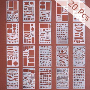 May include: A set of 20 stencils for journaling and crafting. The stencils are made of a silver-colored material and feature various shapes, banners, and lettering. The text "20 PCS" is visible in the image. The stencils include the words "HOPE" and "LOVE".