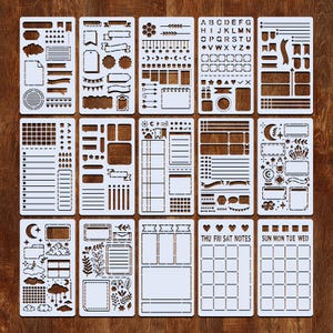 Puede incluir: Un conjunto de plantillas de pl&aacute;stico blanco con varios dise&ntilde;os para bullet journaling y manualidades. Las plantillas incluyen formas, pancartas, calendarios y alfabetos. Las plantillas est&aacute;n dispuestas sobre una superficie de madera marr&oacute;n.