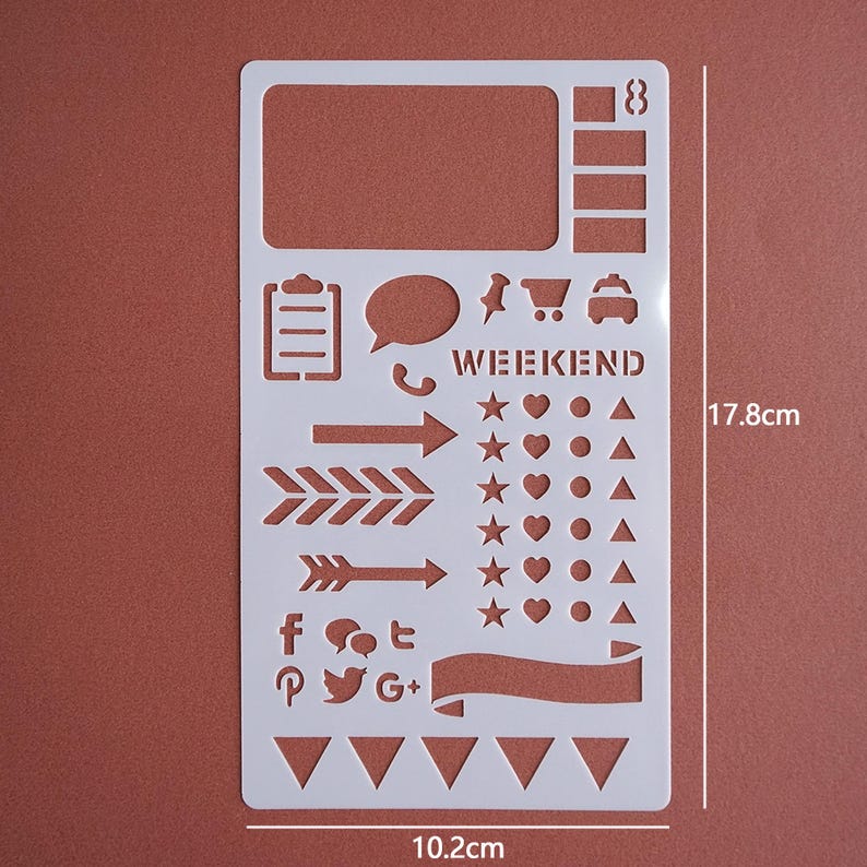 May include: A white plastic stencil with various shapes and icons for journaling or crafting. Includes shapes like arrows, stars, hearts, speech bubbles, and social media logos. The stencil is 17.8cm (7 inches) tall and 10.2cm (4 inches) wide, with the word "WEEKEND" printed on it.