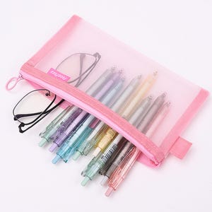 May include: A pink mesh pencil case with a zipper, containing several colorful pens and a pair of eyeglasses. The pens are in various pastel colors, including blue, green, purple, and yellow. The text "PROGFREE" is printed on a pink label.