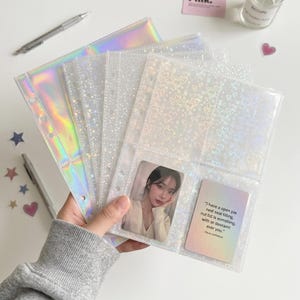以下が含まれることがあります： 星やハートの模様が入ったホログラフィック仕上げの透明なプラスチック製バインダー用リフィルセット。リフィルには複数のポケットがあり、1つのポケットには人物の写真が、もう1つのポケットには「I have a open pie neal seal tilling, nut tid is somshing, with or deoramt ever you.」というテキストが書かれたカードが入っています。