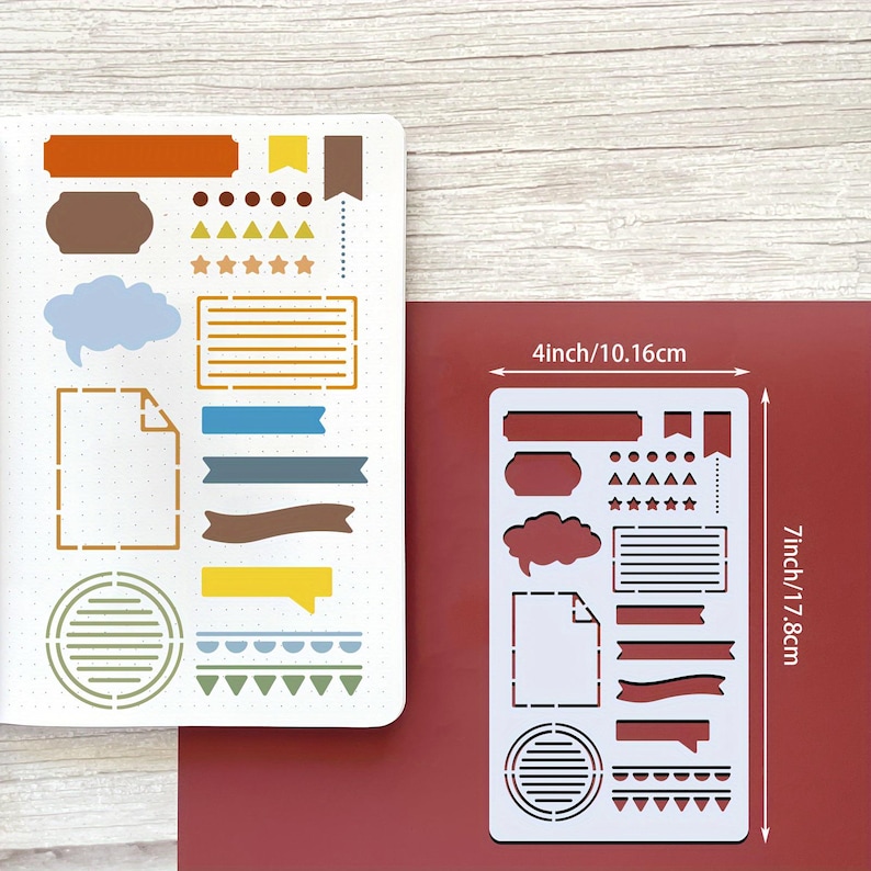 Puede incluir: Una plantilla de pl&aacute;stico blanco con varias formas para journaling, incluyendo banners, bocadillos y estrellas. La plantilla mide 10,16 cm de ancho y 17,8 cm de largo. La plantilla est&aacute; sobre una superficie roja.