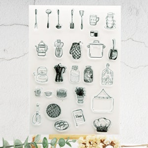 May include: Clear stamp set featuring various kitchen-themed illustrations. Includes utensils, cookware, a chef's hat, and a recipe book. The stamps are in a simple black and white line art style, perfect for crafting and scrapbooking projects.