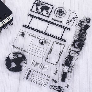 May include: Clear acrylic stamps with travel-themed designs, including a world map, compass, film strip, postcards, and postage stamps. Text includes "Destination," "Card Postal," "Explorer," and "Voyage."
