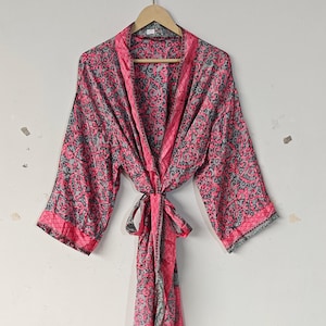 May include: A pink and gray patterned robe hanging on a wooden hanger. The robe has a floral design and a tie closure. The sleeves are long, and the trim is a solid pink. The robe is made of a lightweight fabric.