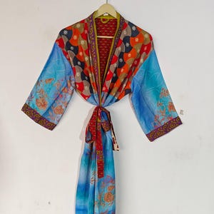 May include: A long, blue and red patterned robe with a floral print on the sleeves and bottom. The robe has a tie belt and is made of silk.