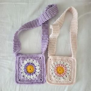 May include: Two handmade crochet bags with daisy designs. One is lavender with a white, purple, and yellow daisy. The other is light pink with a white, pink, and yellow daisy. Both have matching straps.