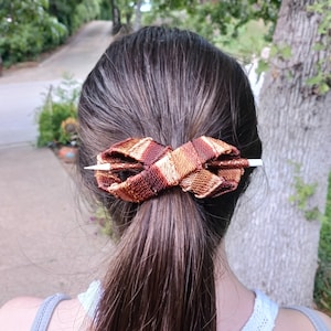 May include: A brown and gold patterned hair stick with a white tip, holding a ponytail in place.