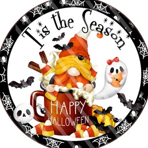 May include: A round, black and white sign with a spiderweb border. The sign says "Tis the Season" with a gnome in a red and orange hat holding a mug of hot chocolate with candy corn and a ghost beside him. The mug says "Happy Halloween".