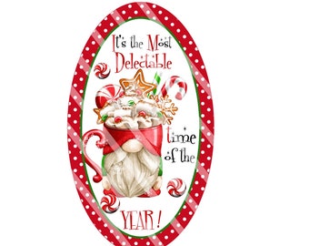 May include: Red and white oval sign with a gnome wearing a red mug with marshmallows, candy canes, and cookies on top. The sign says "It's the Most Delectable Time of the Year!"