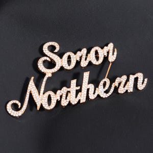 May include: Gold-tone brooch with the words "Soror Norther"n" set in sparkling rhinestones.