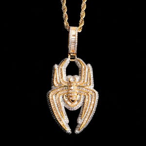 May include: A gold-colored pendant necklace featuring a spider design, encrusted with numerous small, clear gemstones. The spider pendant is suspended from a gold rope chain, creating a luxurious and eye-catching piece of jewelry.