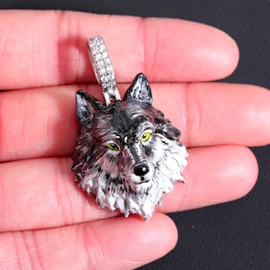 May include: A silver wolf head pendant with a black and white enamel finish and yellow eyes. The pendant is surrounded by a halo of small clear stones.