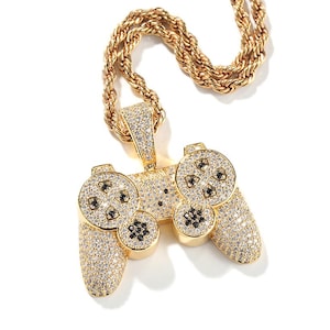May include: Gold-toned pendant necklace featuring a video game controller design. The controller is encrusted with clear and black crystals, and is suspended from a gold rope chain. The pendant has a detailed design with buttons and directional pads.