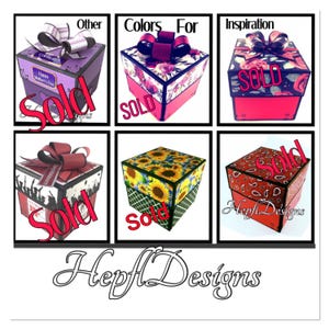 May include: A collection of decorative gift boxes with various designs, including floral, sunflower, and paisley patterns. Each box features a ribbon and the word "Sold" is displayed across the front. The boxes are in different colors, such as pink, red, and purple.