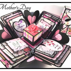 May include: A pink and black explosion box with a floral design and the text "Happy Mother's Day". The box is decorated with lace, hearts, and flowers.