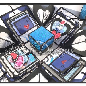 May include: A blue and black explosion box with a blue and white patterned cube in the centre. The box is decorated with hearts, butterflies, and swirls. The box is open and the layers are visible.