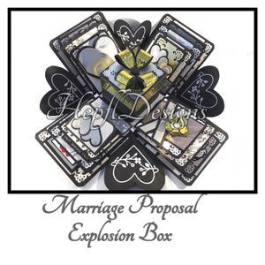 May include: A black and silver explosion box with a gold and black gift box inside. The box is decorated with hearts, flowers, and lace. The text "Marriage Proposal Explosion Box" is printed below the box.