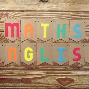 Pode incluir: Uma faixa colorida com as palavras "MATHS ENGLISH" em um arco-íris de cores. Cada letra está em uma bandeirinha de papel marrom separada.