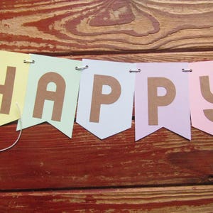 Pode incluir: Uma faixa de cores pastel com a palavra "HAPPY" escrita em letras marrons. Cada letra est&aacute; em uma bandeira separada com a parte inferior pontiaguda.