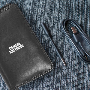 May include: A black leather case with the text "CAMERA BATTERIES" printed on it, a black USB cable, and a black audio cable.