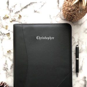 May include: Black leather portfolio with a silver embossed name "Christopher" on the front.
