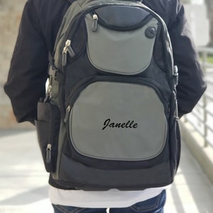 May include: A black and gray backpack with a large front pocket and the name "Janelle" embroidered on it.