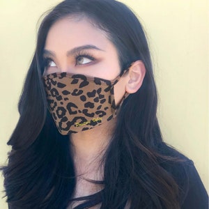 May include: A brown and black leopard print face mask with the text "Positive Vibes" in yellow.